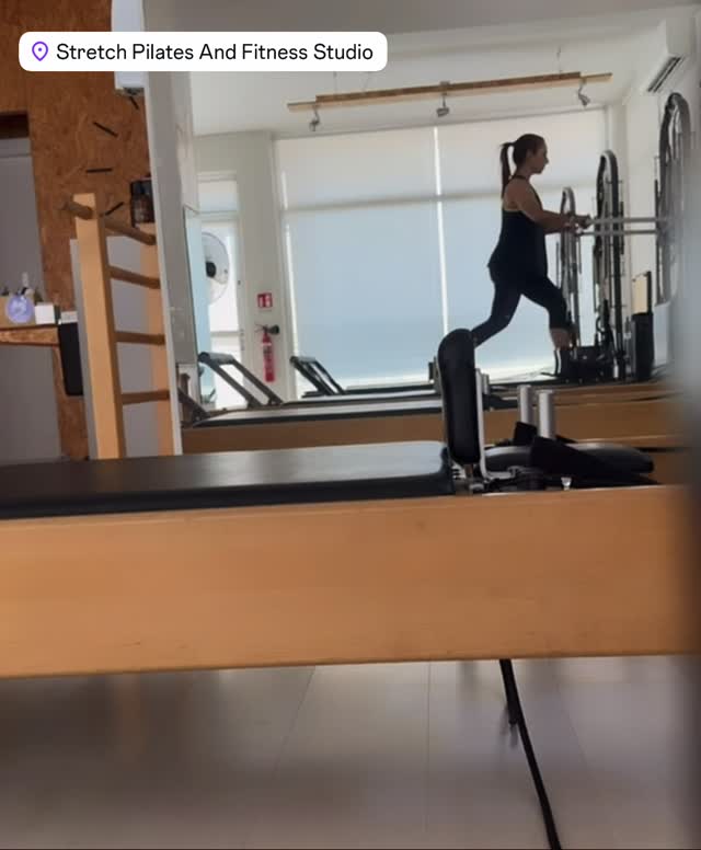 Inside a Pilates studio with a woman exercising on reformer machines reflected in a large wall mirror